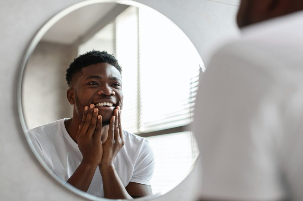 Happy African American Man Touching Unshaven Chin Standing In Bathroom