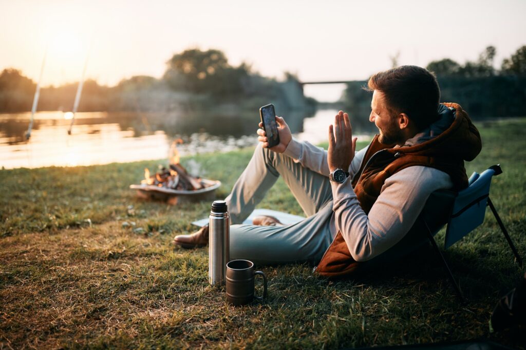 Happy man having video call over smart phone while camping by the lake.