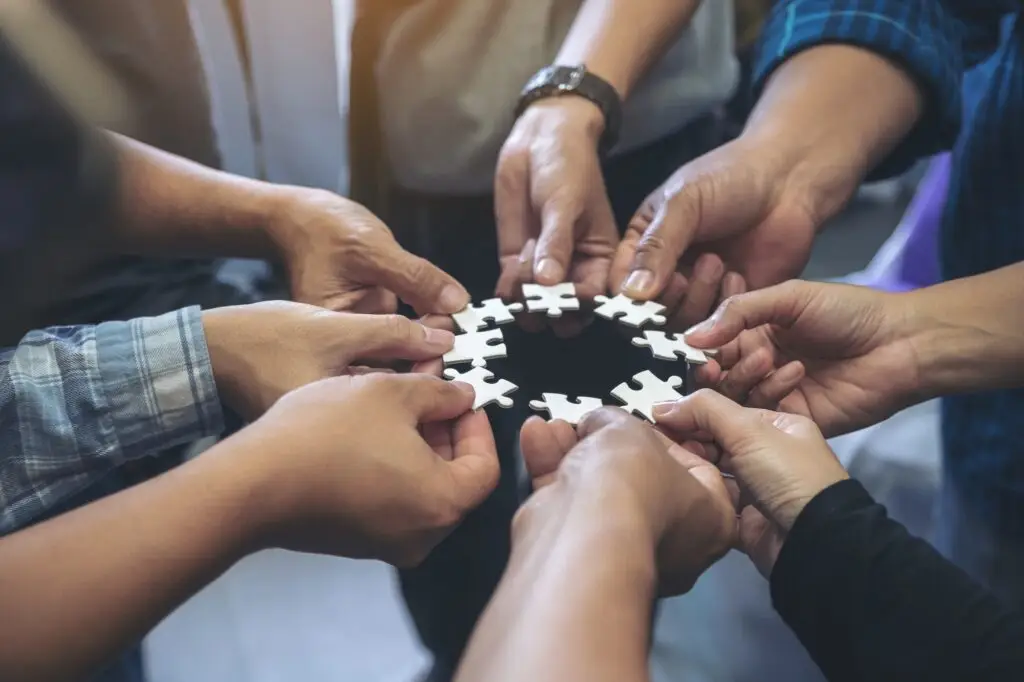 many people hands holding a jigsaw puzzle in circle together