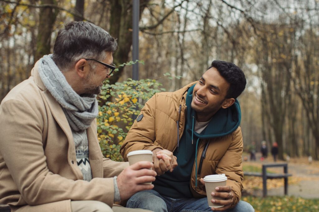 Smiling multiethnic men talking on bench in autumn park