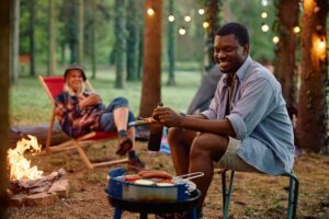 Happy black man making barbecue while camping with his girlfriend in nature.