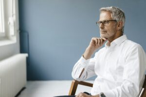 Manager sitting in chair in his office, looking out of the window, thinking